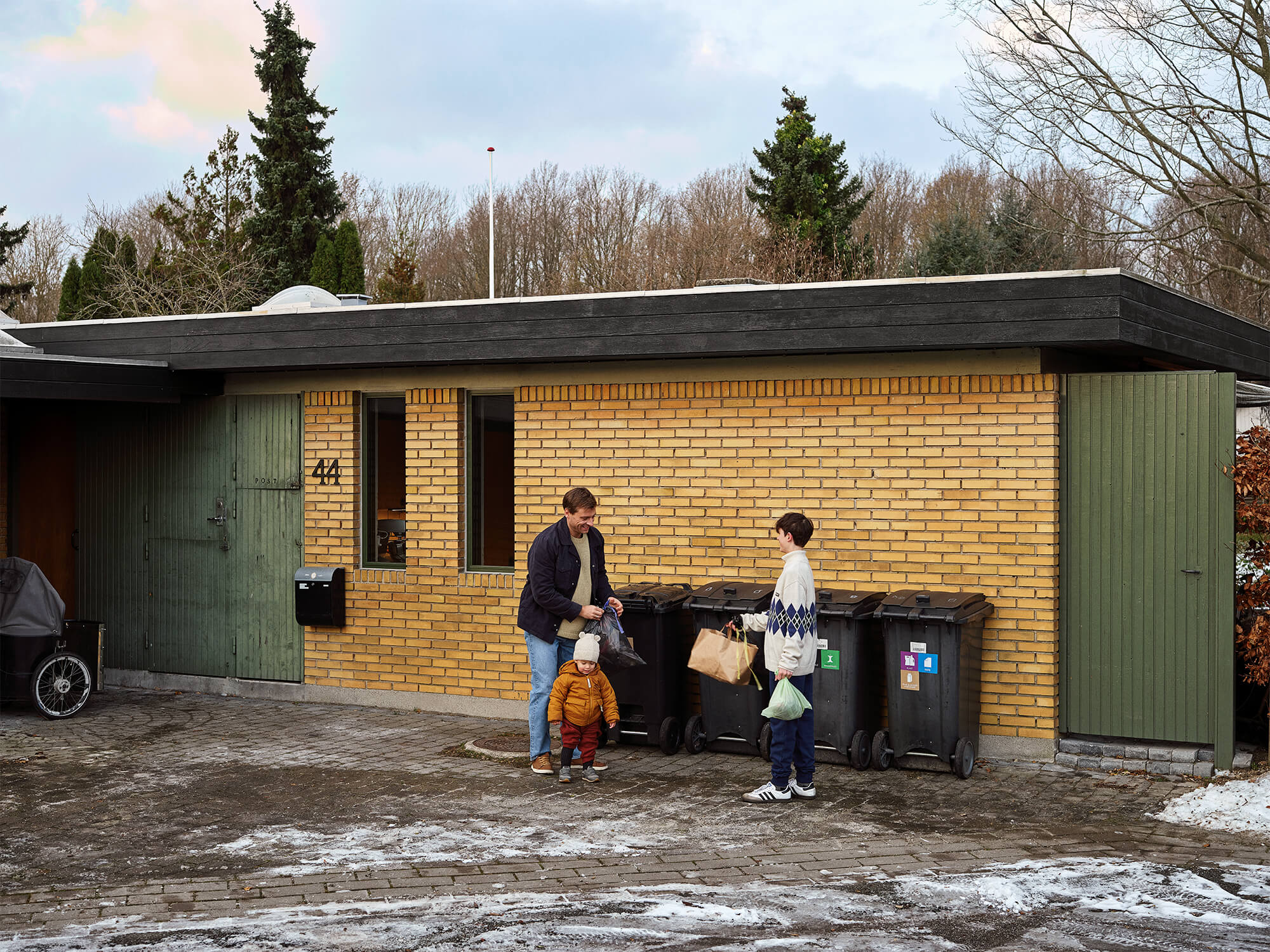 Affaldsspande foran en villa, en voksen og to børn sorterer affald