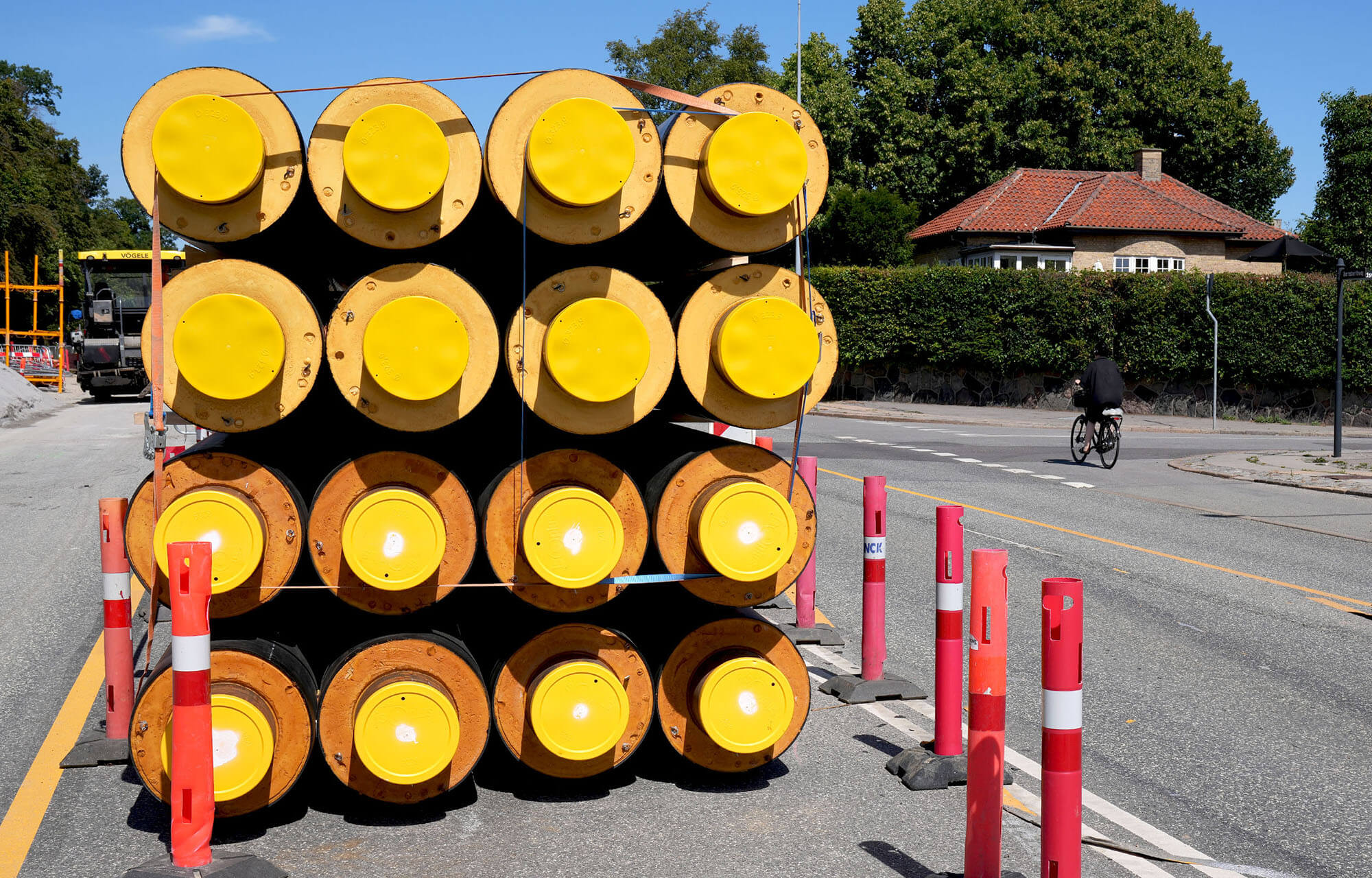 Stablede gule fjernvarmerør på villavej, med cyklist i baggrunden