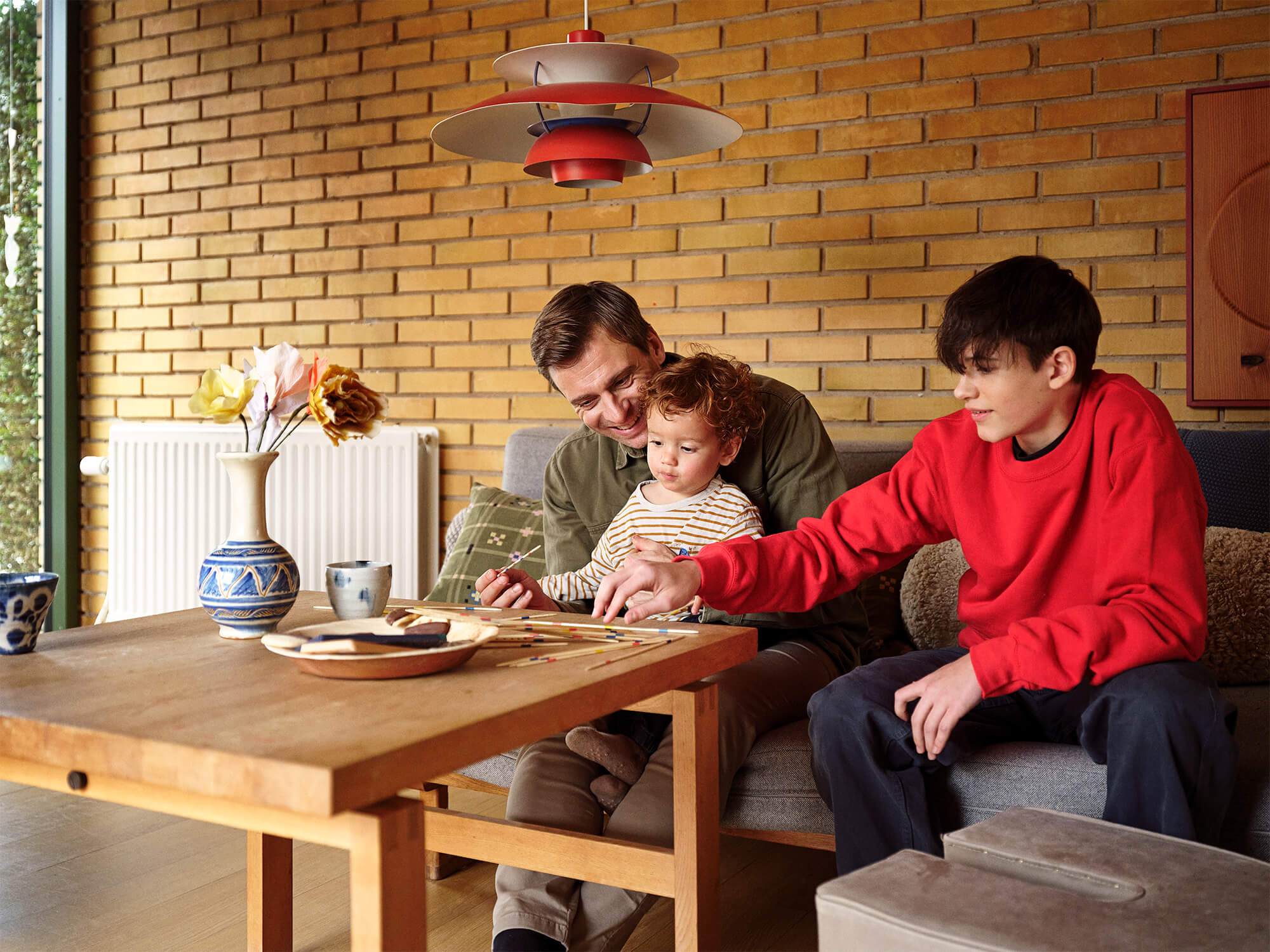 Radiator i en stue, med en voksen og to børn, der spiller mikado