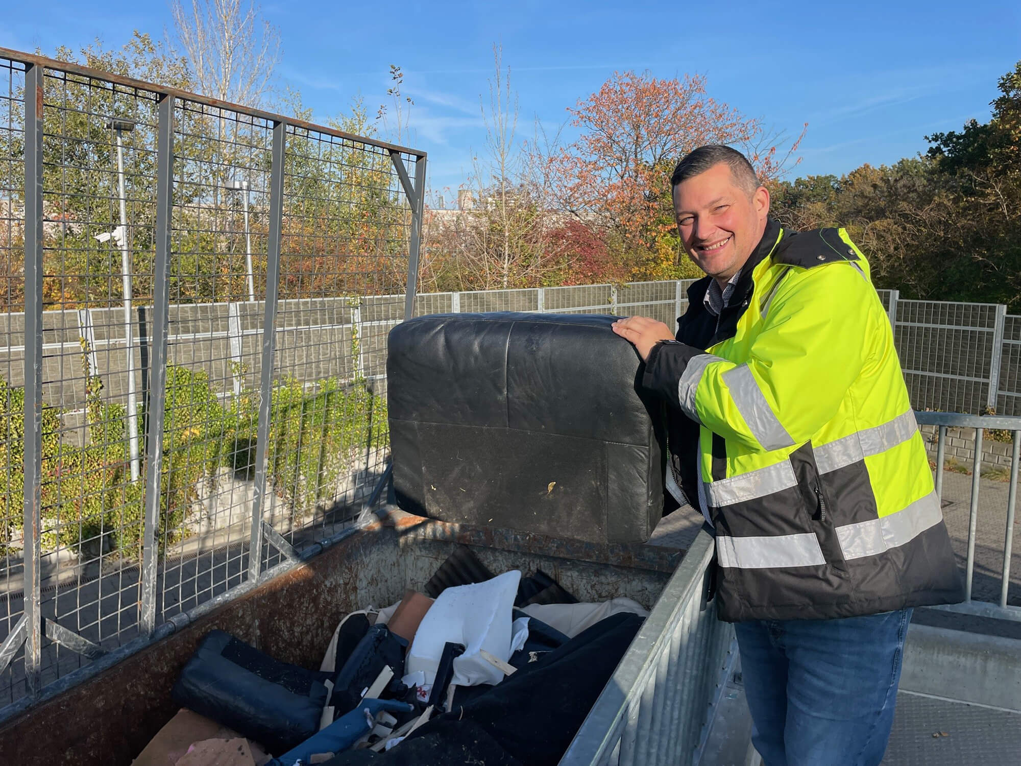 Medarbejder i gul arbejdsjakke på genbrugsstation ved polstrede møbler