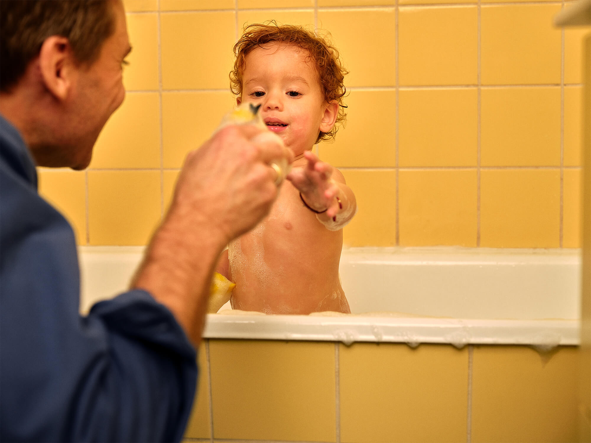 Barn i badekar, voksen med badesvamp som legetøj til barnet